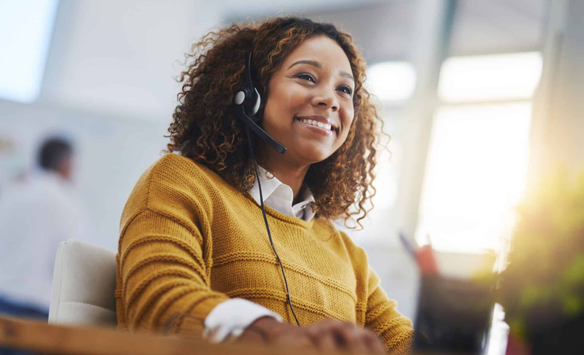 Happy young woman in yellow sweater wearing a headset.