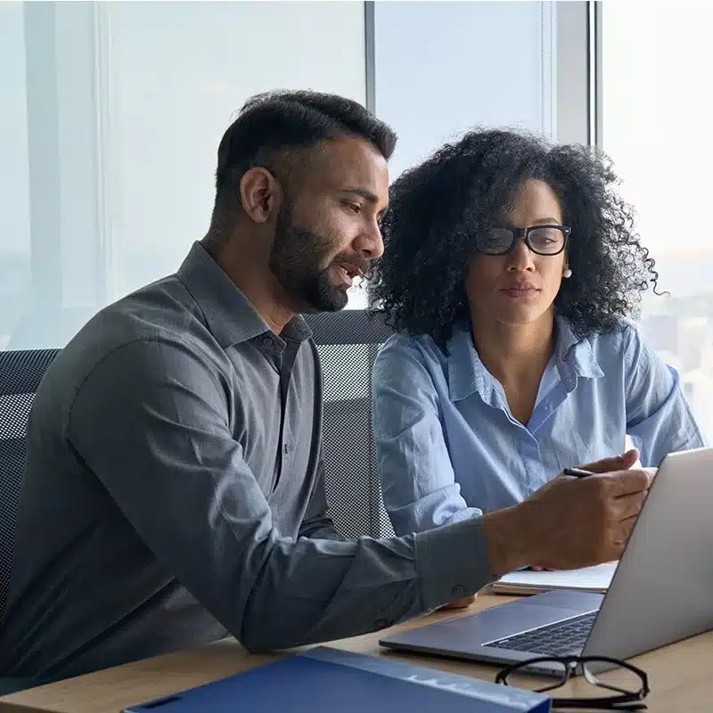 Two colleagues reviewing content on a laptop, discussing and collaborating at a desk.